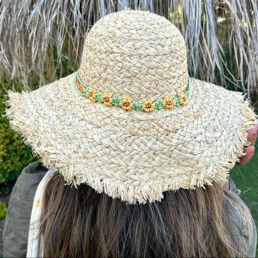 Person wearing a straw hat with a decorative band in front of a thatched umbrella.